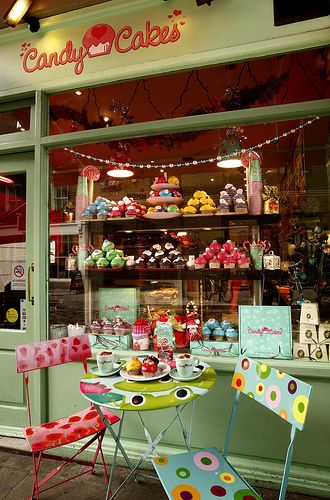 a table and chairs in front of a store window with cupcakes on display