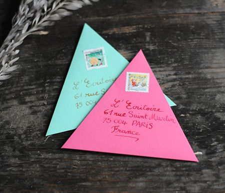 two pink and blue envelopes sitting next to each other on top of a wooden table