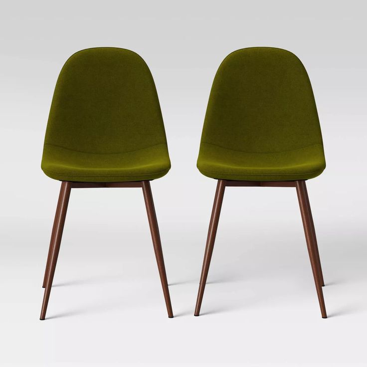 two green chairs sitting side by side in front of a white background and one with wood legs