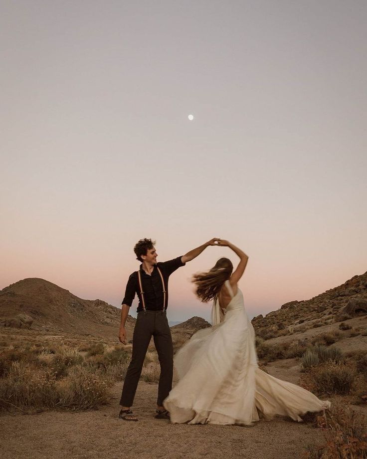 a bride and groom dancing in the desert at sunset with their arms around each other