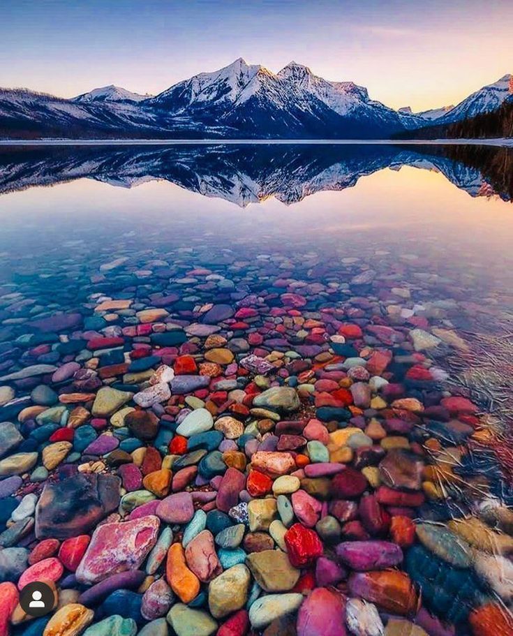 a lake with rocks in the water and mountains in the background at sunrise or sunset