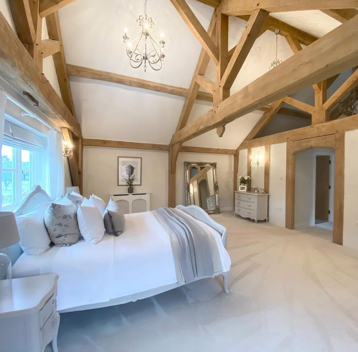 a large white bed sitting inside of a bedroom next to a tall wooden beamed ceiling