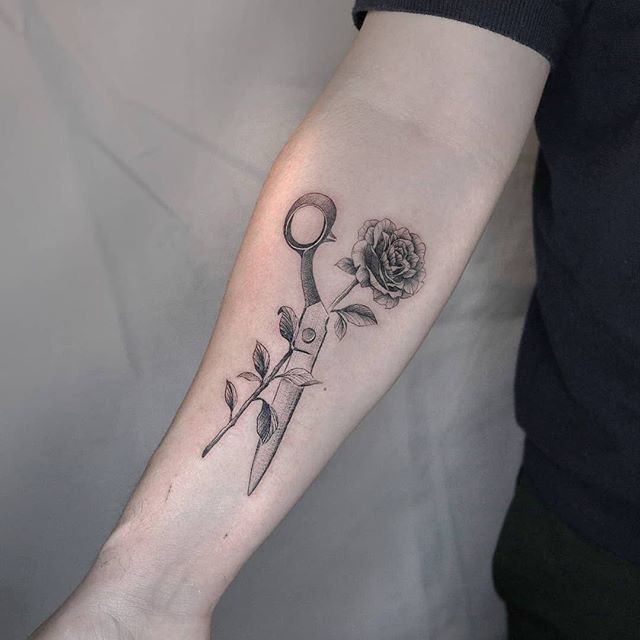 a person with a tattoo on their arm holding a pair of scissors and a rose