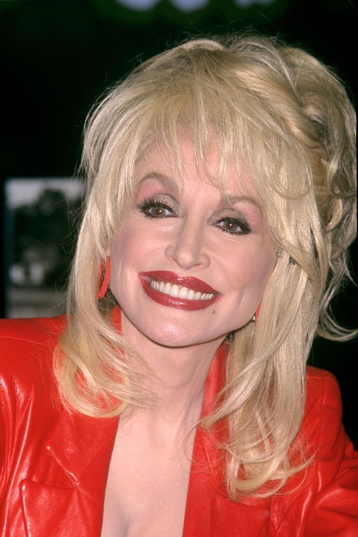 a woman with blonde hair and red leather jacket smiling at the camera while sitting down