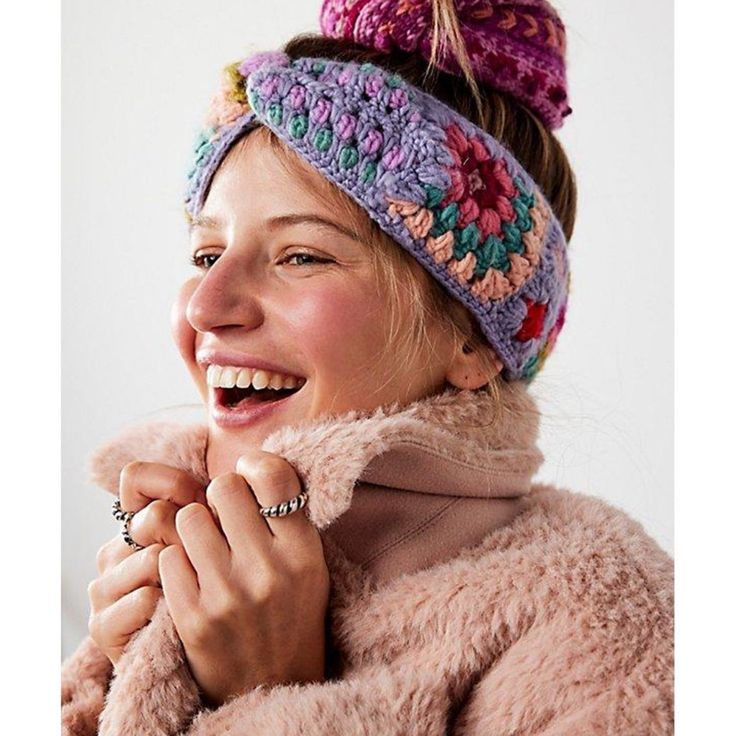 a smiling woman wearing a knitted headband with pompoms on it's sides