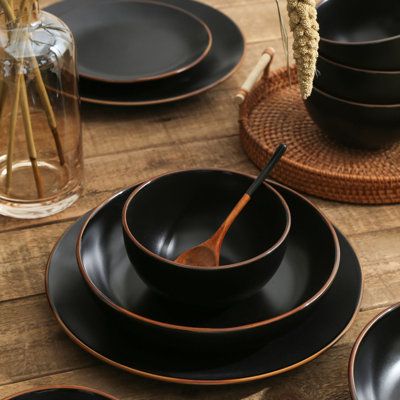 black plates and bowls are arranged on a wooden table with wicker placemats