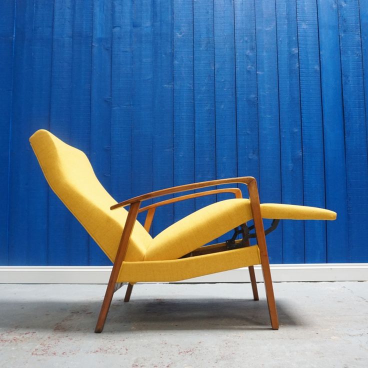 a yellow reclining chair sitting in front of a blue wall with a wooden frame