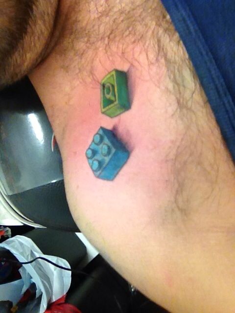 a man with a small tattoo on his chest has a lego piece in the shape of a cube