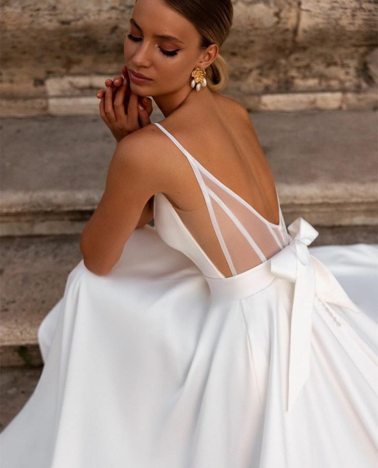 a woman in a white dress is sitting on some steps with her hand under her chin