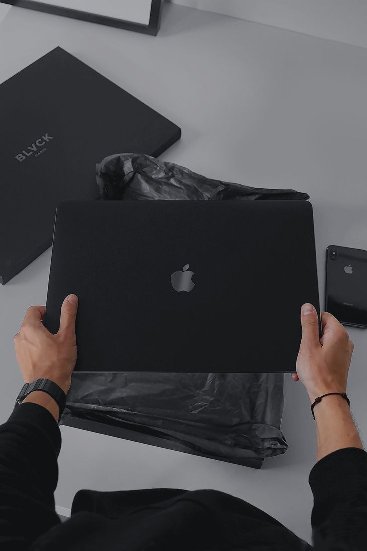 a person holding an apple laptop in their hands on a table next to other items