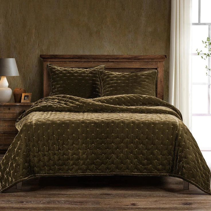 a bed with green bedspread and pillows in a room next to a window