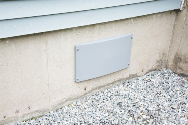 the corner of a house with gravel around it and a metal sign attached to the wall