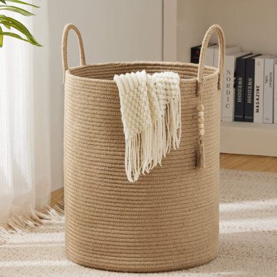 a large round basket with tassels on the sides and handles is shown in front of a bookshelf