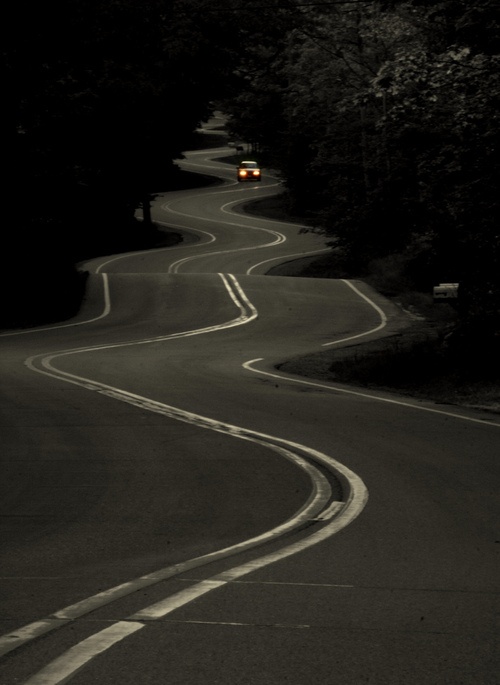 a curved road with two cars driving down it at night in the distance is lit up by street lights