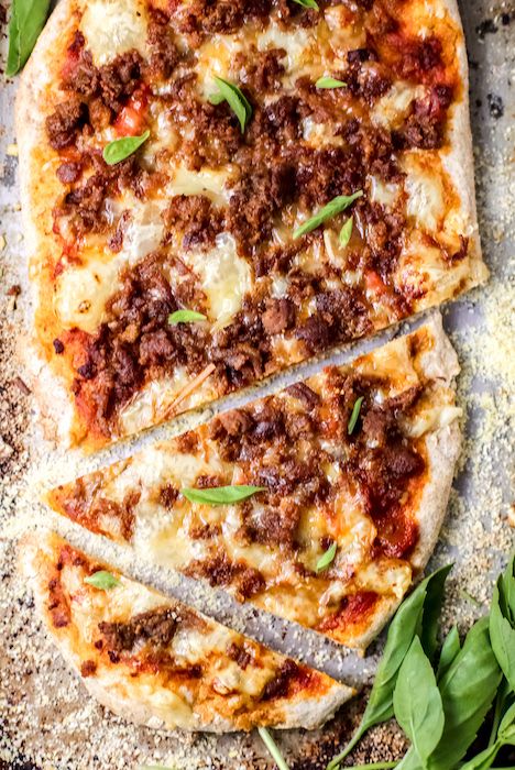 a pizza with meat, cheese and spinach leaves on the table next to it