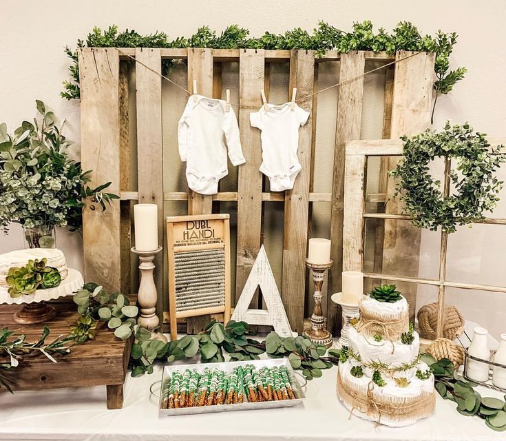 a table topped with lots of baby goods and greenery next to a wooden wall