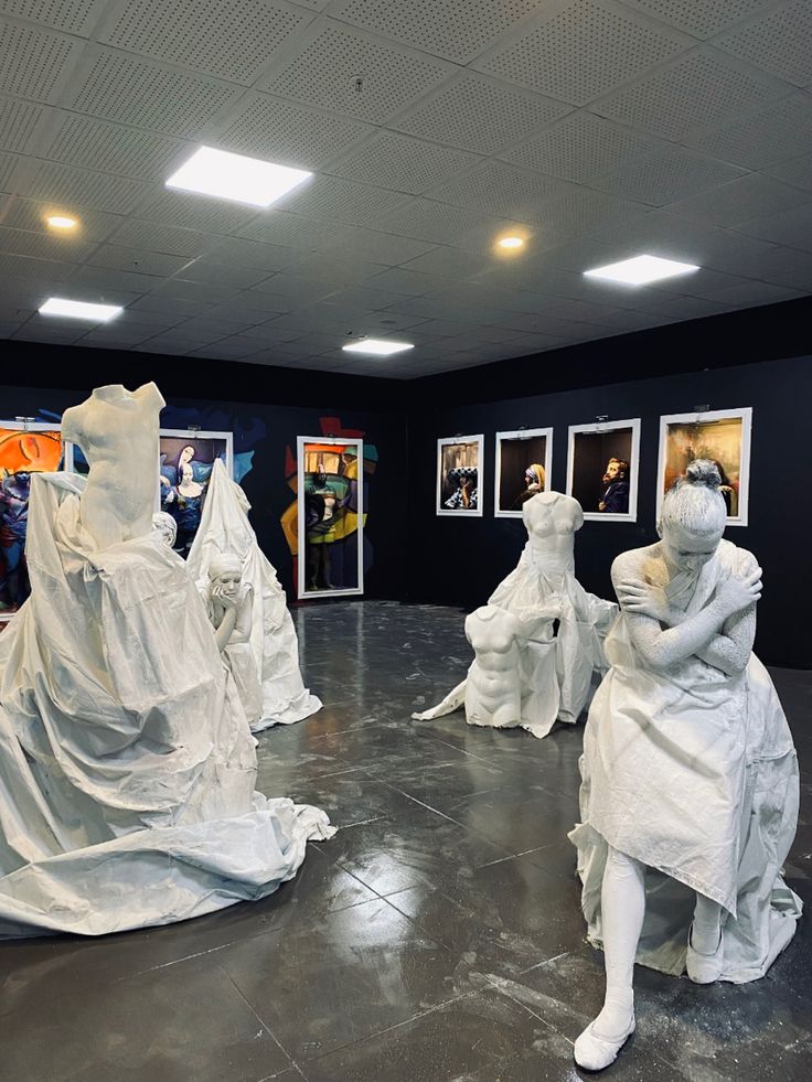 several white sculptures are sitting on the floor in an empty room with black walls and framed pictures