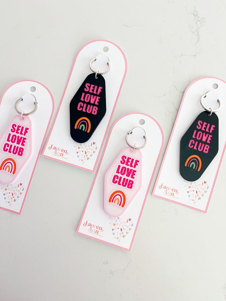 three keychains with self love club designs on them, one has a rainbow and the other says self love club