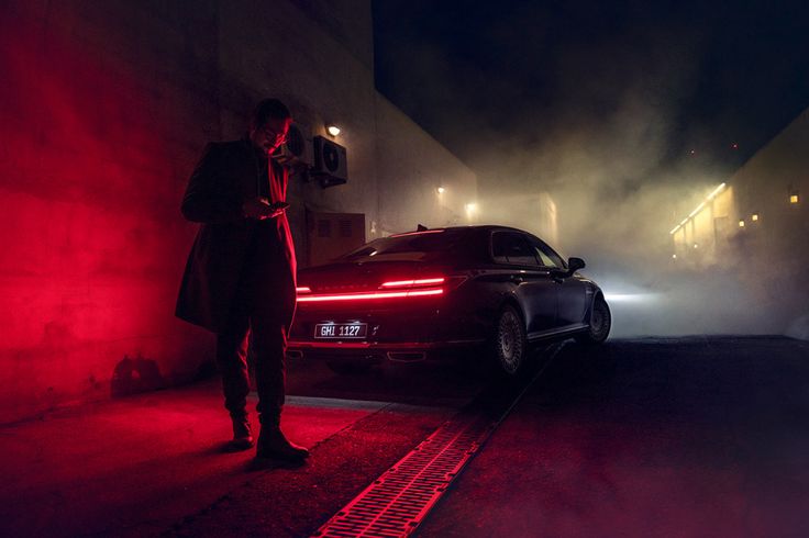 a man standing next to a car in the dark with red light coming from it