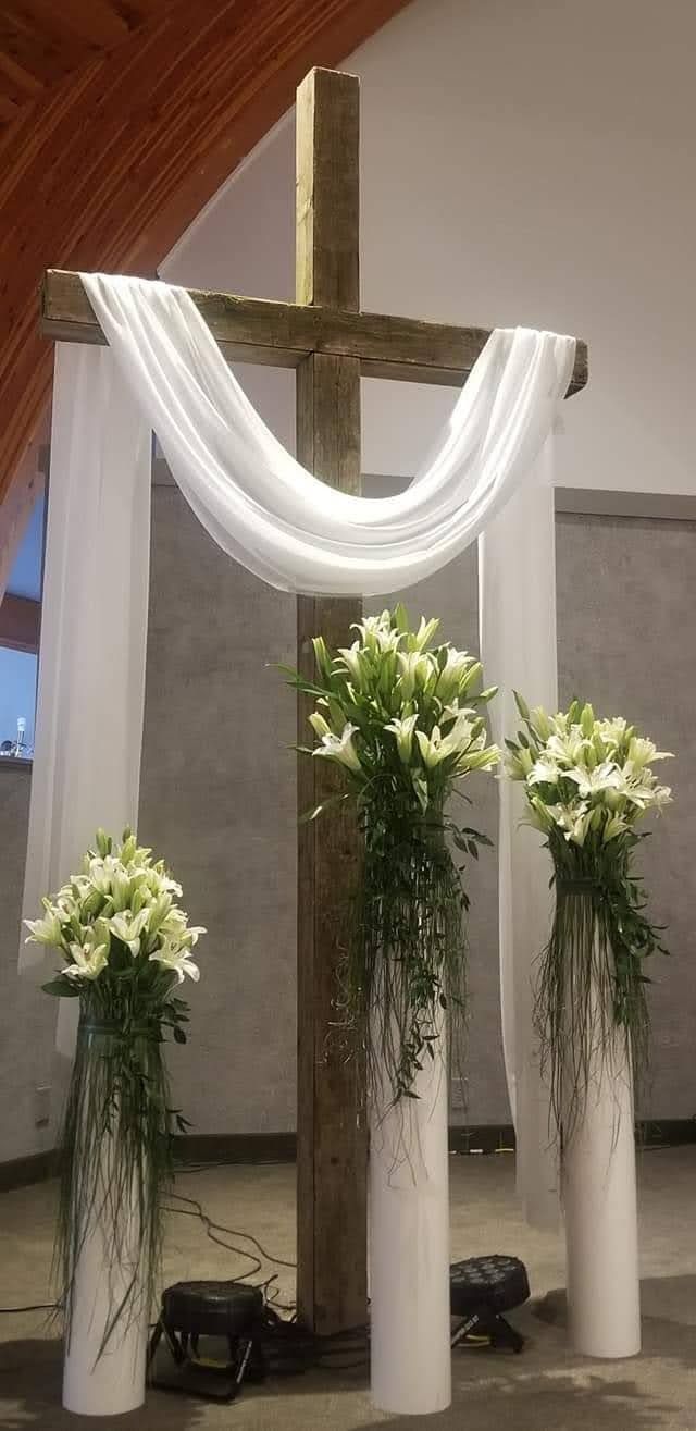 three white vases with flowers in front of a cross