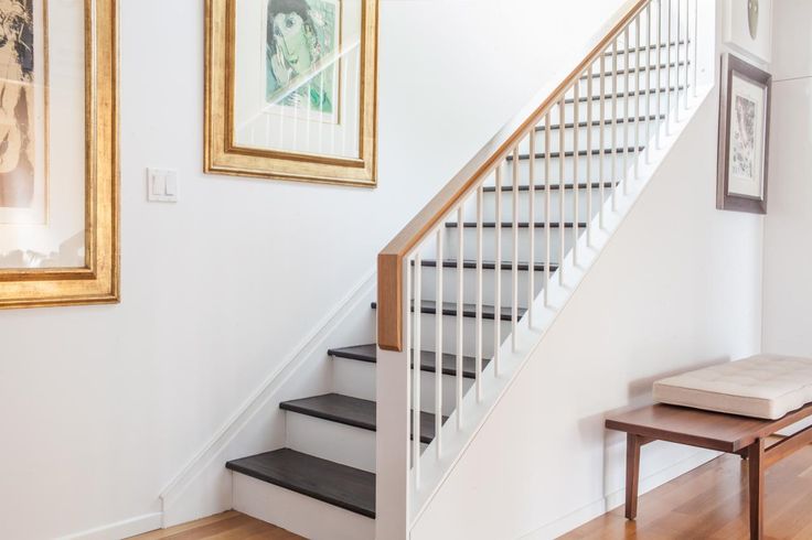 there is a white staircase with black steps in the room and framed pictures on the wall