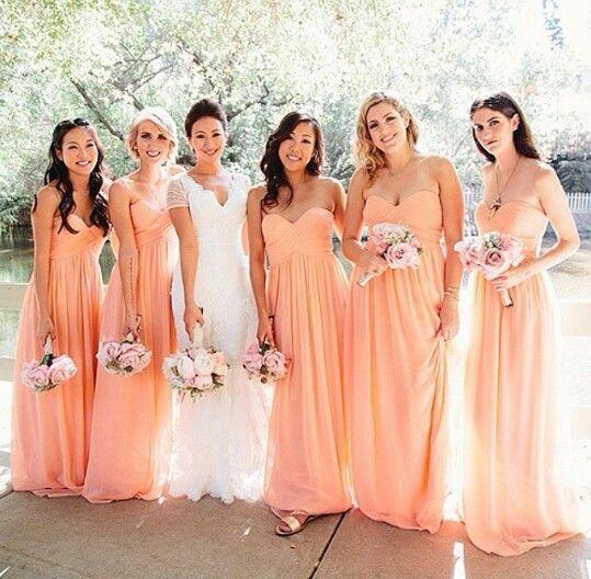 a group of women standing next to each other in long peach colored dresses and holding bouquets