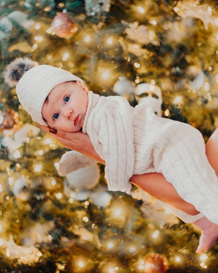 a baby in a white dress and hat hanging from a christmas tree