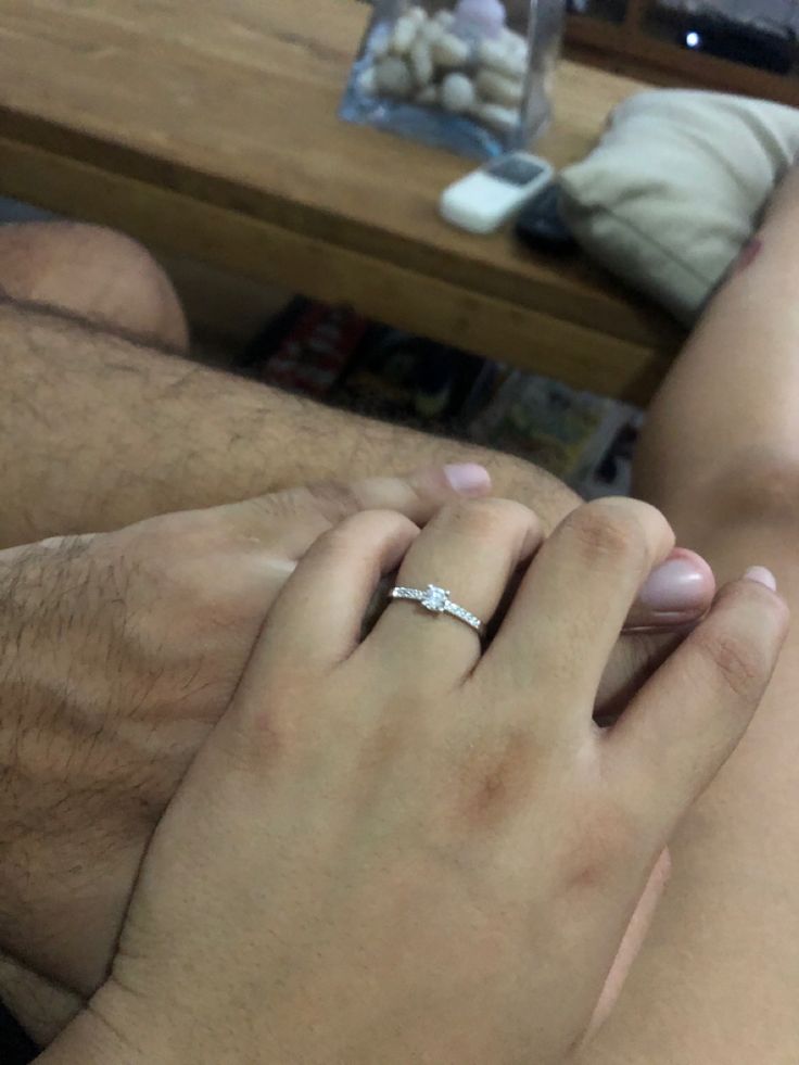 a man and woman holding each other's hand while sitting on a couch in front of a coffee table