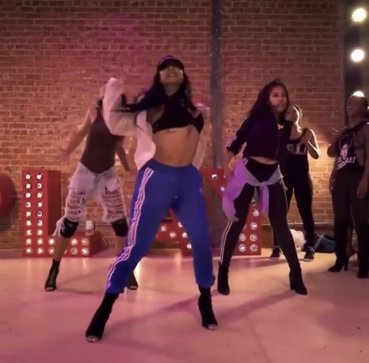 a group of young women dancing on top of a dance floor in front of a brick wall