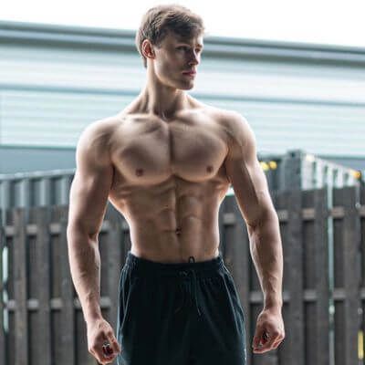 a shirtless man standing in front of a fence with his hands on his hips