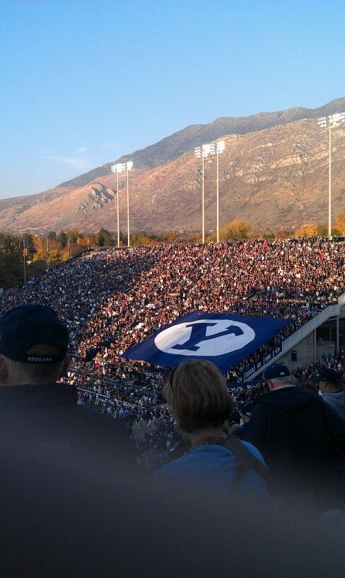 a large group of people sitting in the stands at a football game with mountains in the background