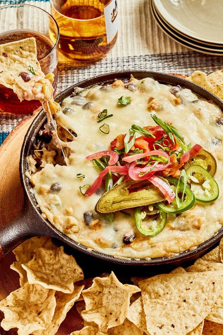 a skillet filled with dip, vegetables and tortilla chips on top of a table