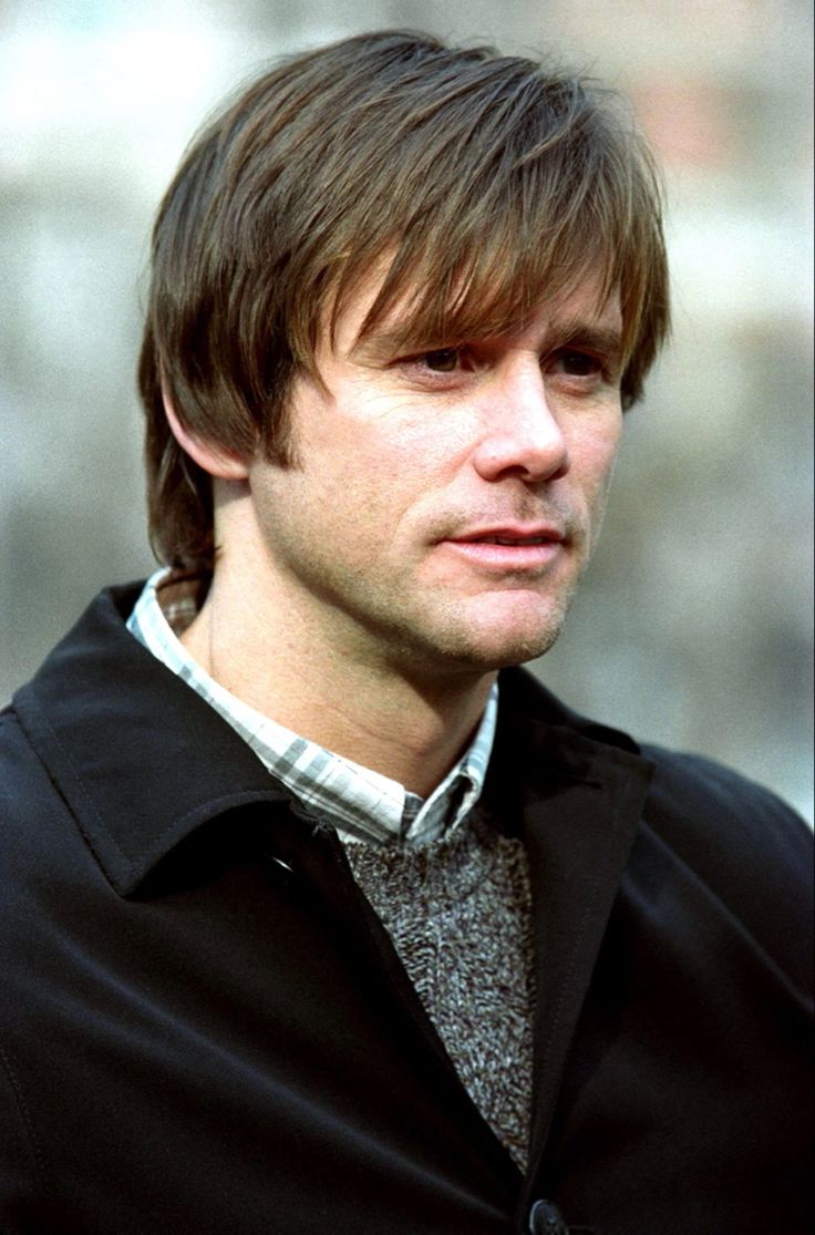 a man with long hair wearing a black jacket and plaid shirt looking at the camera