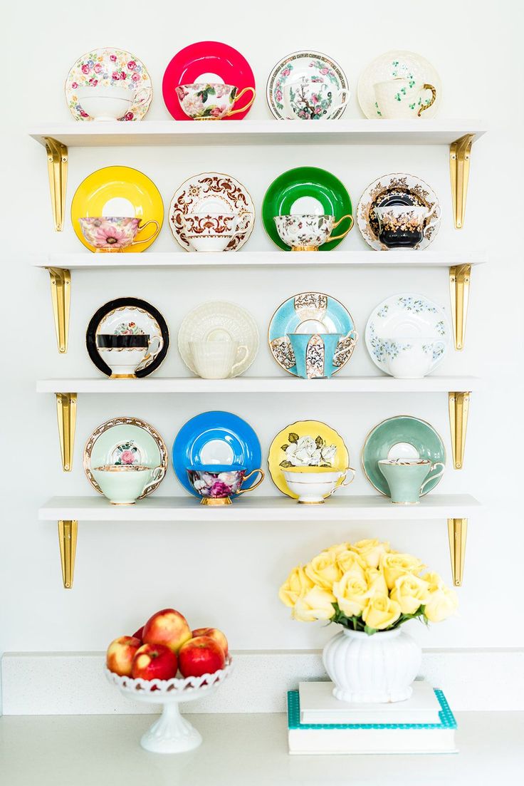 plates and bowls are arranged on the wall above a vase with yellow roses in it