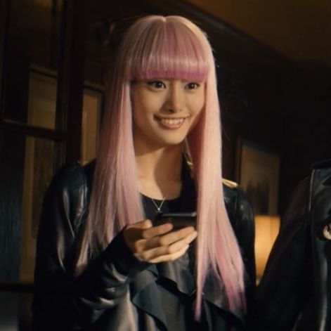 a woman with pink hair is looking at her cell phone and smiling while wearing a black leather jacket