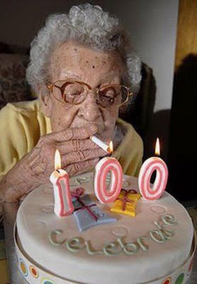 an old woman blowing out candles on her birthday cake with the number 100 written on it