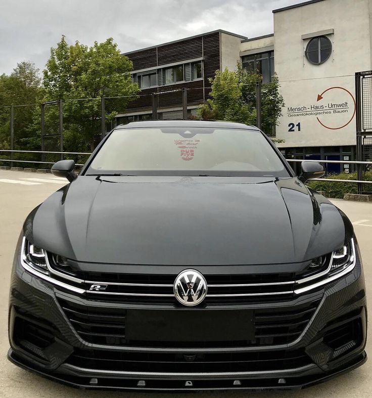 the front end of a black volkswagen sedan parked in front of a building with large windows