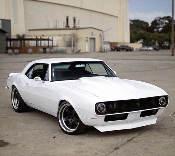 a white muscle car parked in front of a building