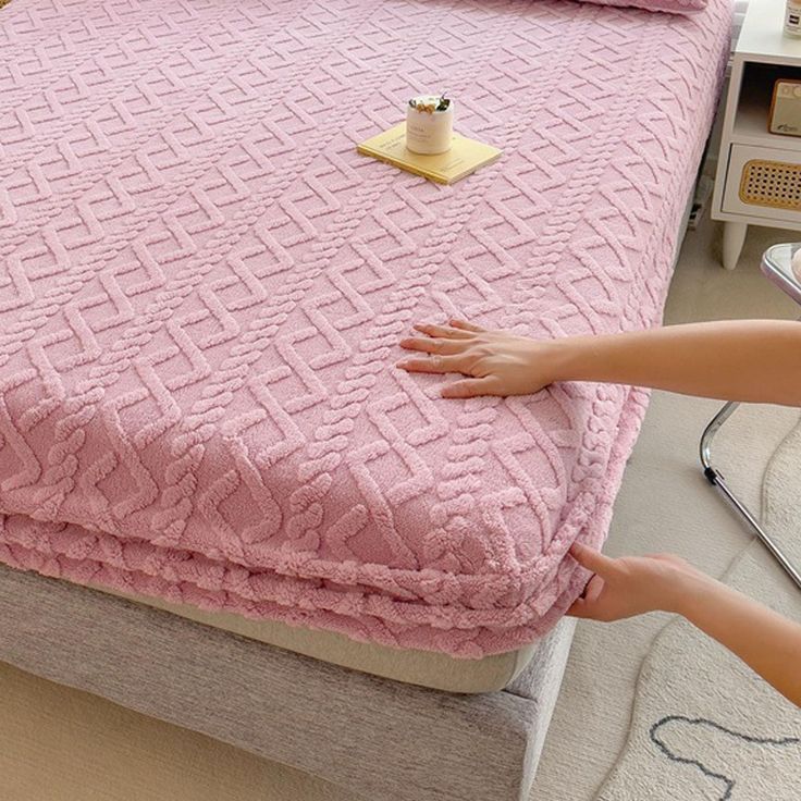 a woman is placing a pink blanket on a bed