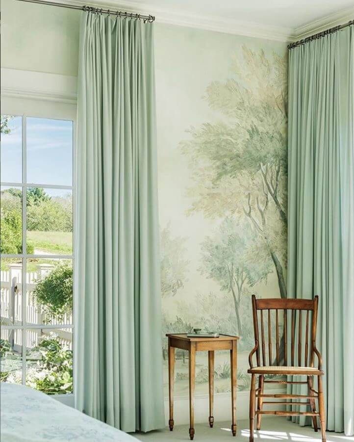 a chair and table in front of a wall with trees painted on it, next to a window