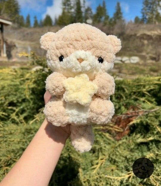 a person holding a teddy bear in their left hand with trees in the back ground