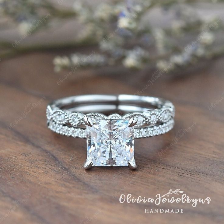 a princess cut diamond engagement ring set on top of a wooden table with flowers in the background