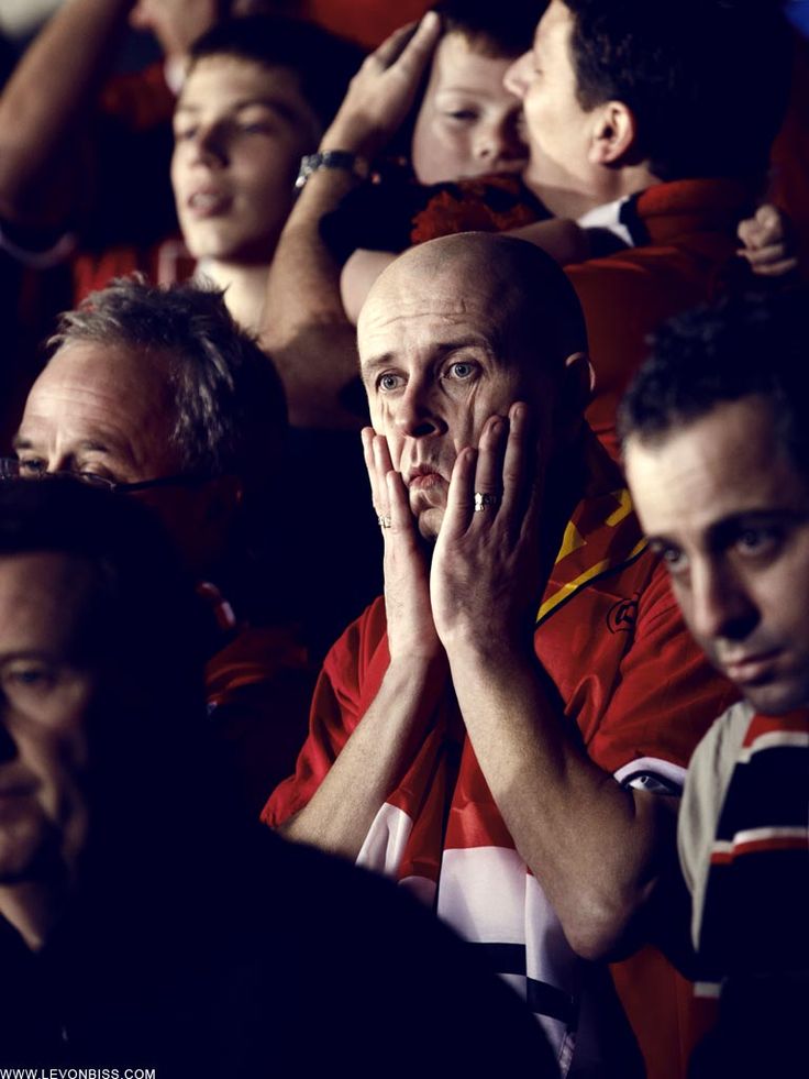 a group of men sitting next to each other at a soccer game with their hands on their face