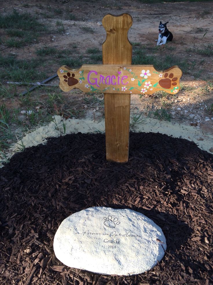 a wooden cross sitting on top of a pile of mulch next to a dog