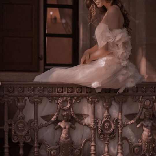 a woman in a white dress sitting on a balcony