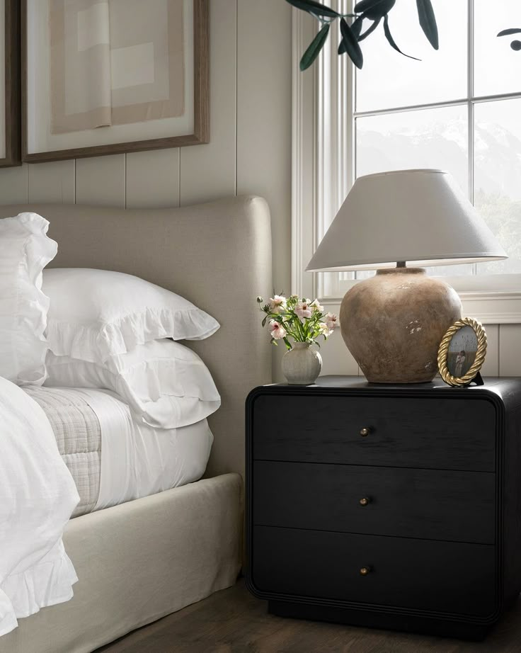 a bed with white sheets and pillows next to a lamp on top of a night stand