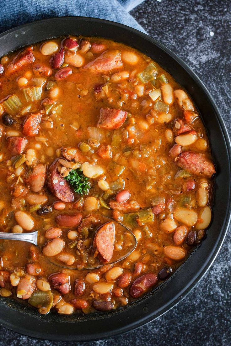 a bowl filled with beans and sausages on top of a table next to a spoon