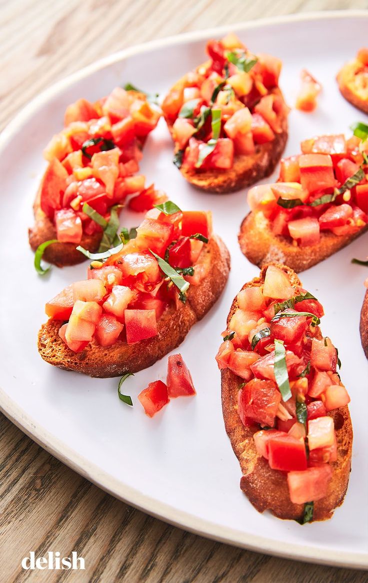 several pieces of bread with tomatoes and basil on them sitting on a white platter