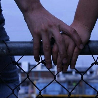 two people holding hands over a fence with the city in the background