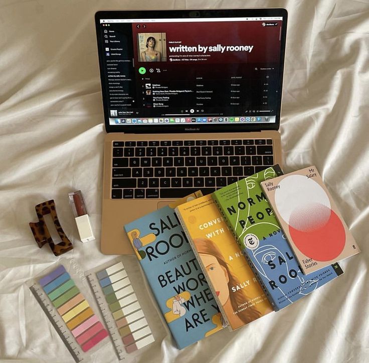 an open laptop computer sitting on top of a bed next to some books and markers